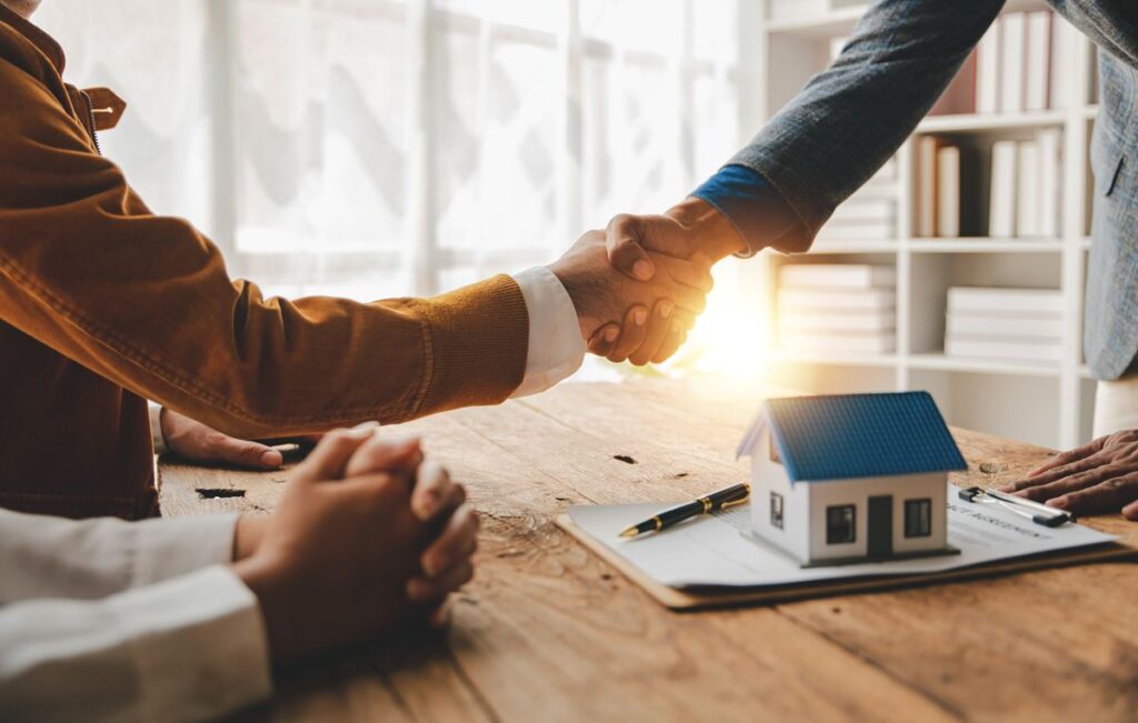 Two people shaking hands over a table with a home loan and miniature house in El Paso, TX