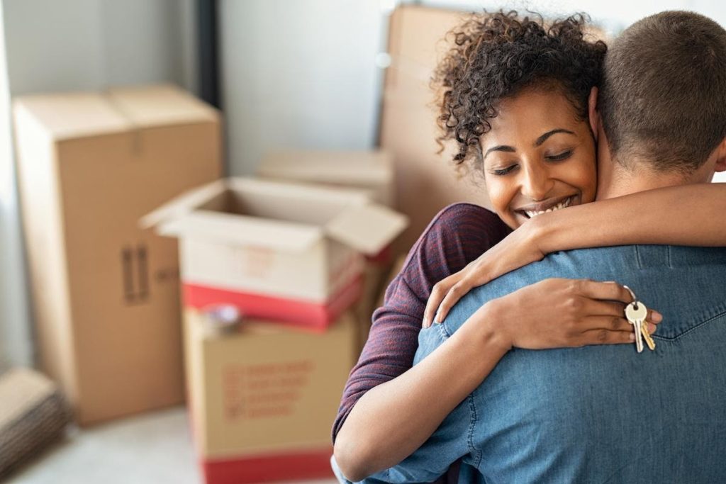 A young couple embracing with moving boxes in the background