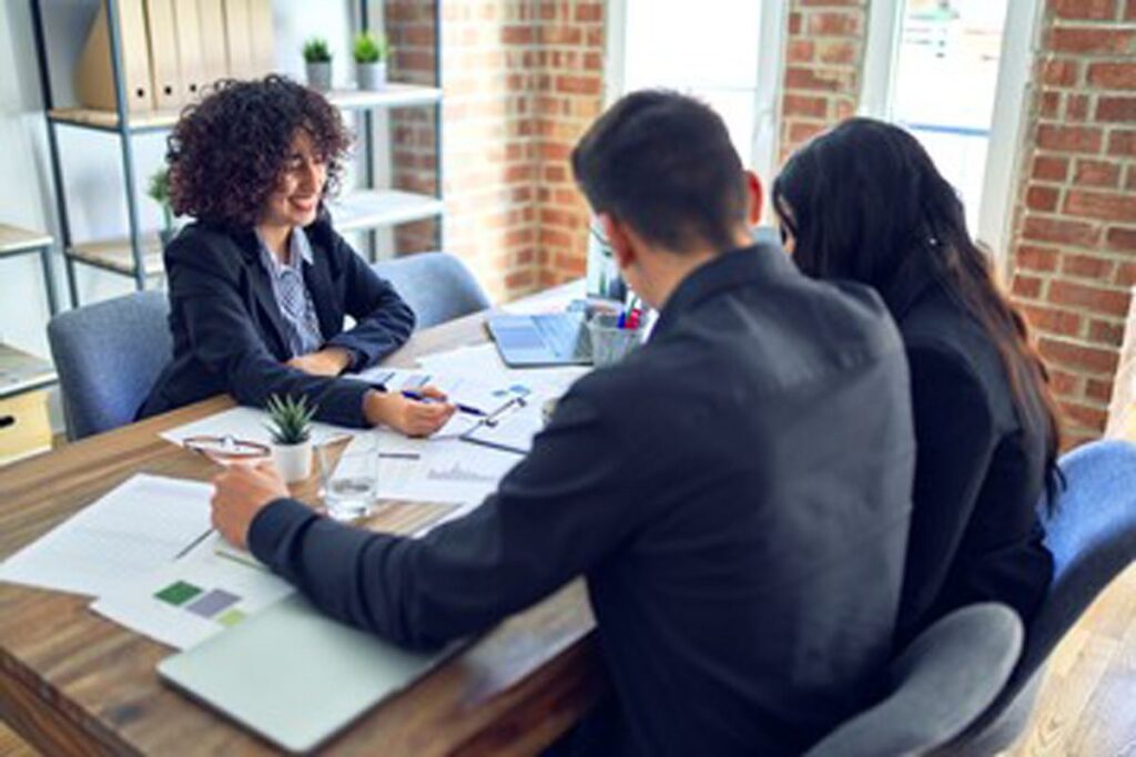 A young couple and a mortgage lender are going over paperwork in El Paso, TX